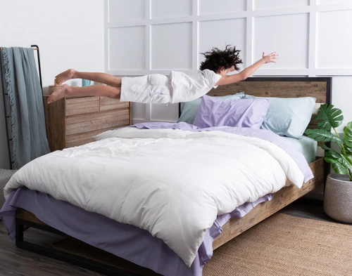 Angled view of a young girl diving into a queen-sized bed dressed in a multi-coloured mix of our Cotton Caress Sheet Sets.