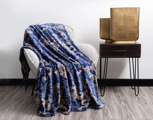 Angled view of our Lucky Dragon Throw in Gold Fortune draped over a modern grey armchair in a white room.