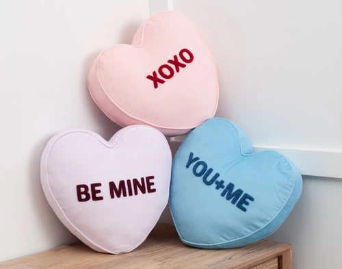 Our XOXO, Be Mine, and You+Me Candy Heart Cushions piled neatly in a bedroom corner on top of a dresser.