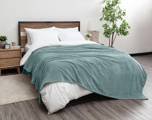 Angled view of our Ocean Chevron Plush Blanket dressed over a white queen bed.