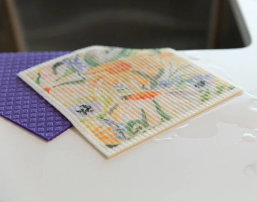 Angled view of our Wildflower Swedish Dishcloth Set absorbing water on a countertop.