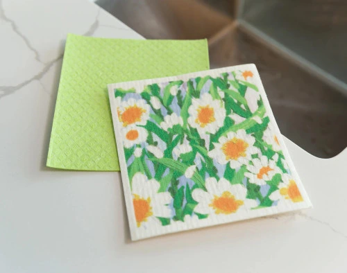 Top view of our Daisy Swedish Dishcloth Set sitting next to a sink on a white marble countertop.