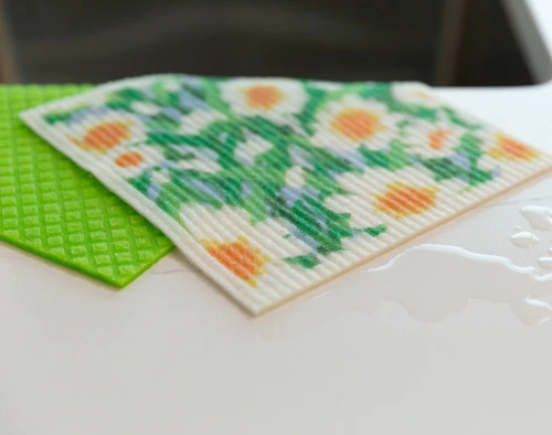 Angled view of our Daisy Swedish Dishcloth Set absorbing water on a countertop.