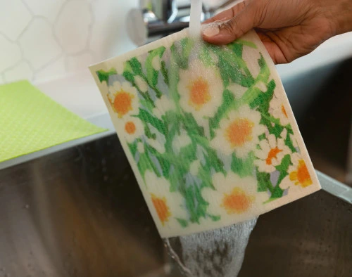 Side view of our Daisy Swedish Dishcloth Set under a sink to be rinsed for reuse.