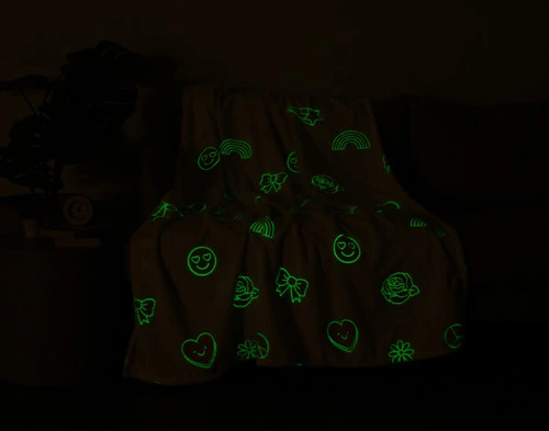 Our Peace & Love Glow in the Dark Fleece Throw sitting with a light green glow in a darkened living room.