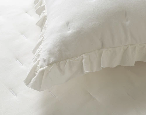 Close-up on the frilled edging on the corner of a pillow sham for our Alessia White Quilt Set.