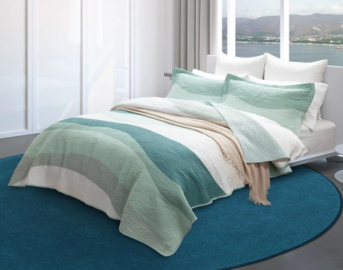 Angled view of our Ocean Waves Cotton Quilt Set in a seaside bedroom with a natural beige blanket.