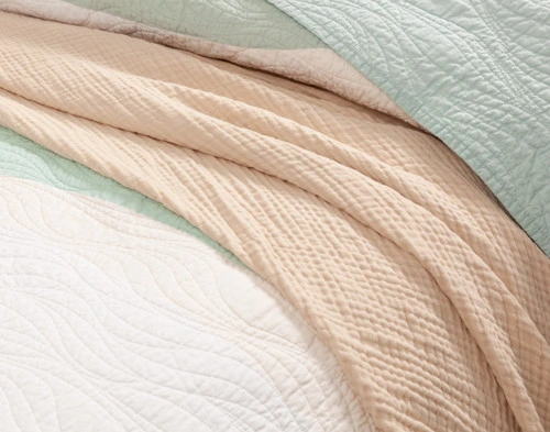 Close-up view of the green and white tones beside a beige blanket on our Ocean Waves Cotton Quilt Set.