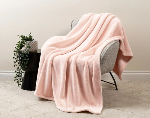 Our Velvet Plush Throw in Powder Pink draped over a beige chair in a white living room.