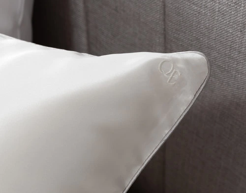 Close-up on the QE Home embroidered logo on the corner of our Snow Mulberry Silk Piped Edge Pillow Sham.