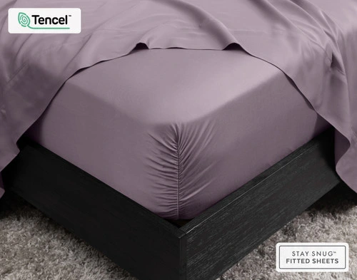 Close-up of the corner on our BeechBliss TENCEL™ Modal Fitted Sheet in Purple Haze snugly fit over a mattress with a flat sheet draped on top.