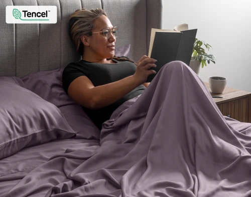 Woman wrapped up in our BeechBliss TENCEL™ Modal Sheet Set in Purple Haze sitting upright and reading a book.