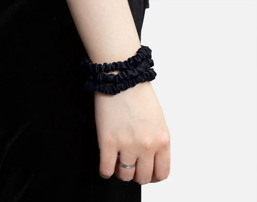 Side view of three Mulberry Silk Scrunchies in Black being worn around an adult's wrist.