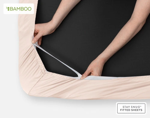 Underside of our Bamboo Cotton Fitted Sheet in Rosemist with two hands stretching the snug fit elastic strands around the corner of a mattress.