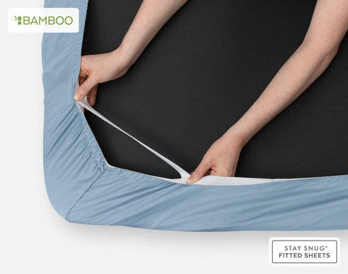 Underside of our Bamboo Cotton Fitted Sheet in Mistral Blue with two hands stretching the snug fit elastic strands around the corner of a mattress.