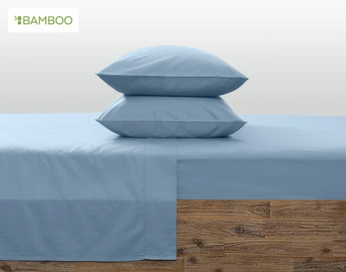 Two pillows in Bamboo Cotton Pillowcases in Mistral Blue stacked on top of each other on a bed with matching sheets.