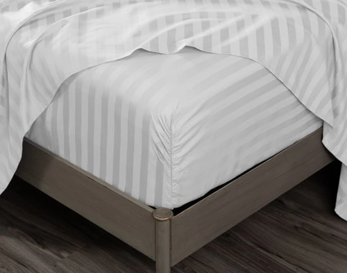 Close-up on the fitted sheet of our White Luxor Egyptian Cotton Sheet Set over a mattress, with a matching flat sheet draped overtop.