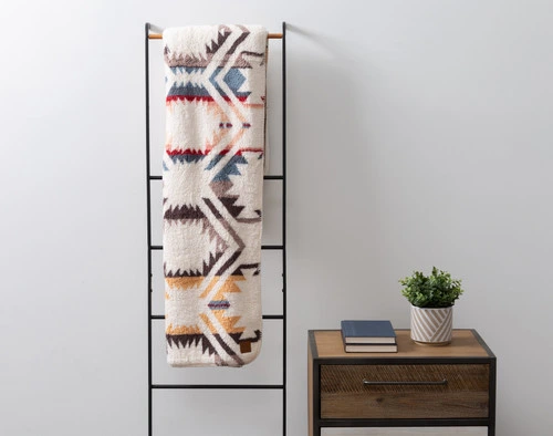 Front view of our Natural Southwest Throw hanging on a rack along the wall of an empty living room.