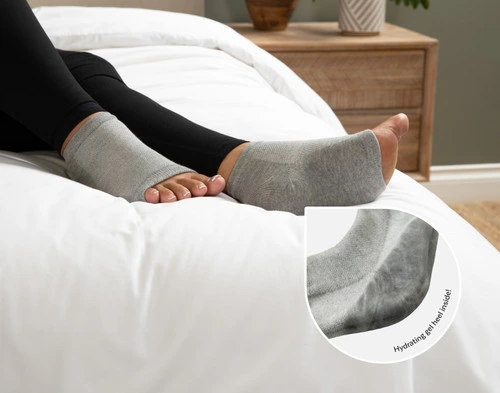 Angled view of a woman's feet wearing our Grey Hydraheel Spa Socks, with a magnifying glass to show the hydrating inner gel heel.