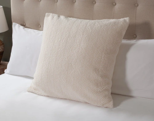 Angled view of our Ripple Boucle Euro Sham in Cream leaning against two white pillows on an undressed bed.