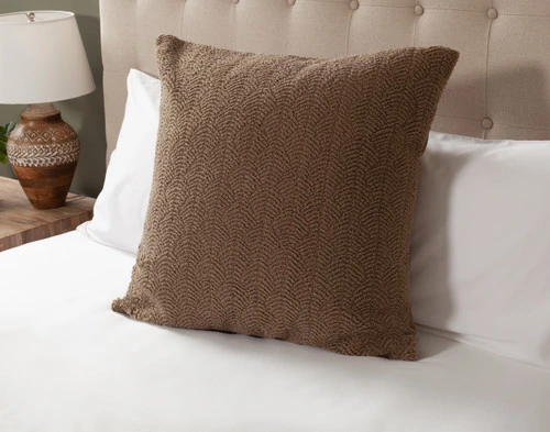 Angled view of our Ripple Boucle Euro Sham in Truffle leaning against two white pillows on an undressed bed.