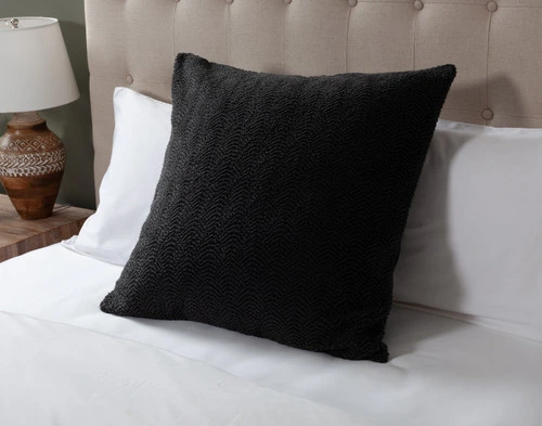 Angled view of our Ripple Boucle Euro Sham in Soot leaning against two white pillows on an undressed bed.