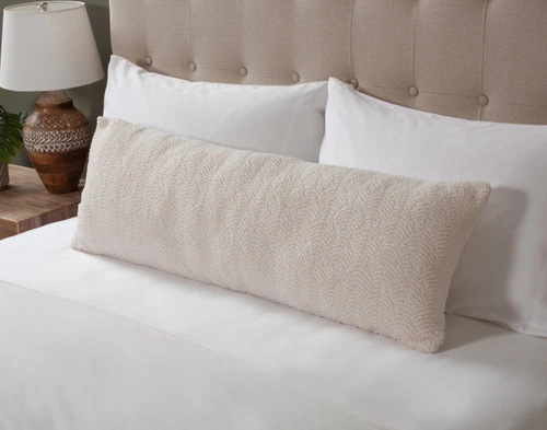 Angled view of our Ripple Boucle Lumbar Pillow in Cream leaning against two white pillows on an undressed bed.