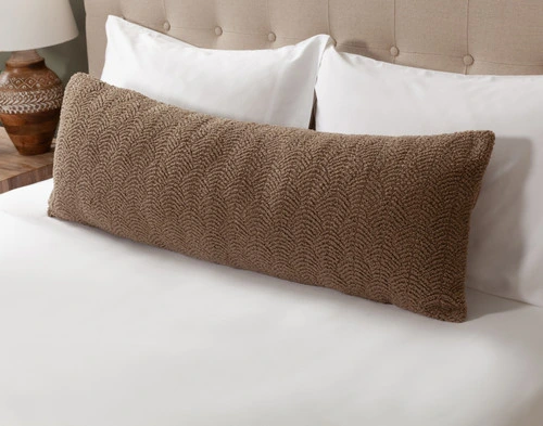 Angled view of our Ripple Boucle Lumbar Pillow in Truffle leaning against two white pillows on an undressed bed.