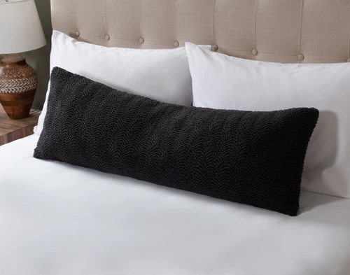 Angled view of our Ripple Boucle Lumbar Pillow in Soot leaning against two white pillows on an undressed bed.