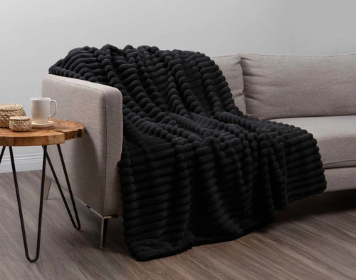 Angled view of our Black Channel Plush Throw draped over a light grey couch in an empty modern living room.