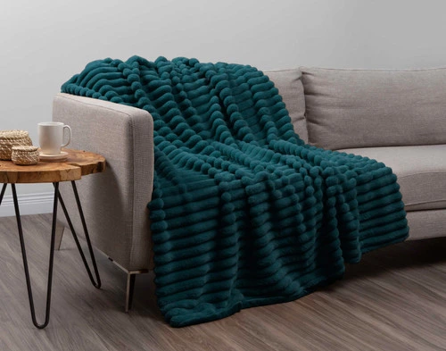 Angled view of our Deep Sea Channel Plush Throw draped over a light grey couch in an empty modern living room.