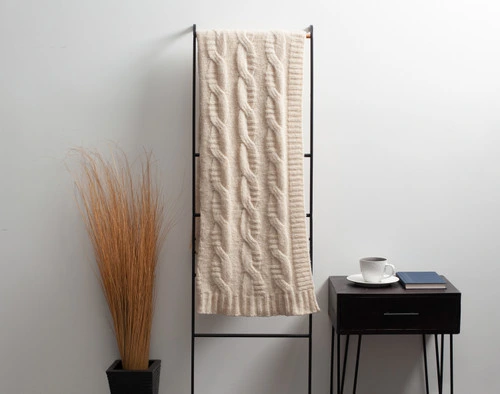 Front view of our Cream Fisher Knit Throw hanging on a tall rack against a solid white wall.