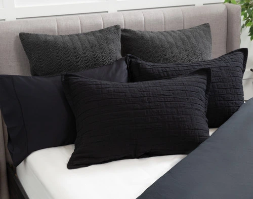 Angled view of our Jetset Black Pillow Sham sitting against coordinating pillows on a half-dressed white bed.