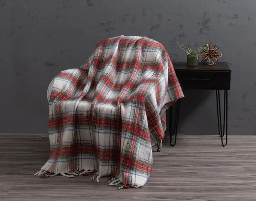 Angled view of our Holiday Plaid Mohair Throw draped over a small chair in a grey room.