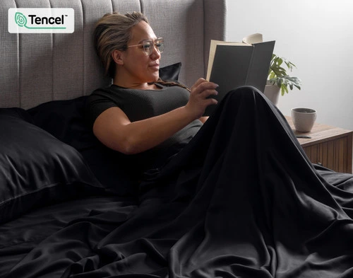 Woman wrapped up in our BeechBliss TENCEL™ Modal Sheet Set in Black reading a book while sitting upright.