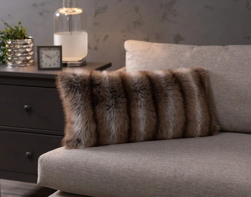 Angled view of our Mink Sable Faux Fur Boudoir Pillow sitting on the  edge of a couch in a dark modern bedroom.