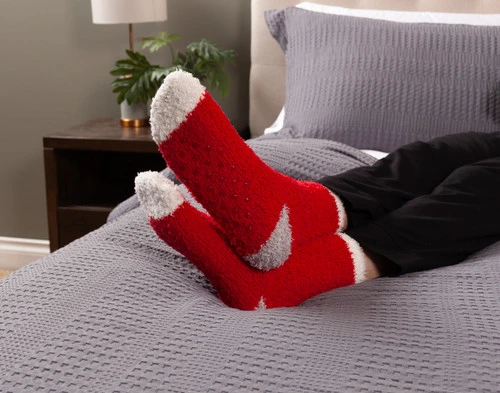 Bottom view of two feet wearing our Red Lounge Socks resting on a bed.