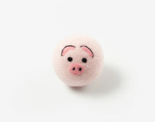 Front view of our Piggy Embroidered Wool Dryer Ball sitting on a solid white surface.