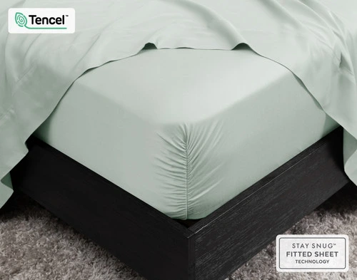 Close up of the BeechBliss Tencel Modal Sheet Set in light green Waterfall on the corner of a black bed, featuring the fitted sheet and the flat sheet.