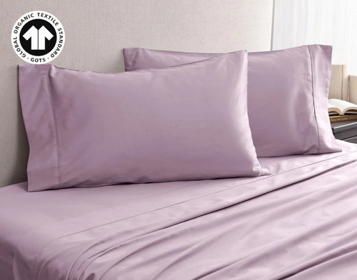 Angled view of our Organic Cotton Pillowcases in Amethyst, resting on an empty bed with matching sheets.