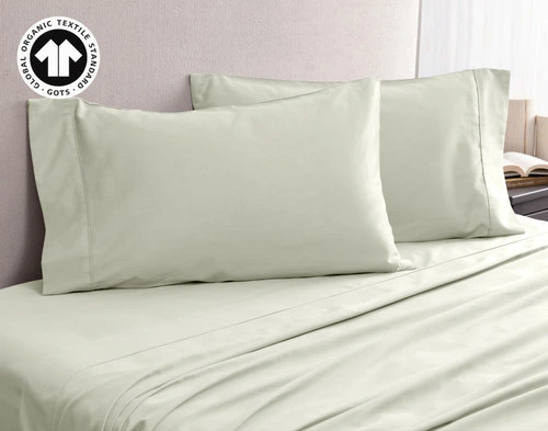 Angled view of our Organic Cotton Pillowcases in Sagebrush, resting on an empty bed with matching sheets.