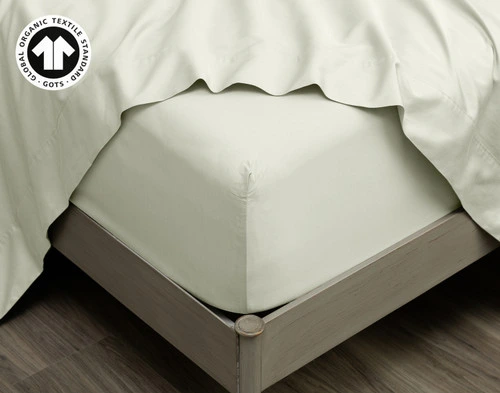 Our Organic Cotton Fitted Sheet in Sagebrush at the corner of a bed with the matching Flat Sheet on top.