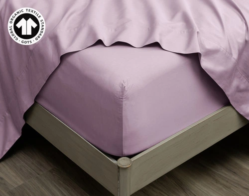 Our Organic Cotton Fitted Sheet in Amethyst at the corner of a bed with the matching Flat Sheet on top.