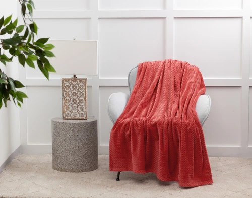 Our Chevron Plush Throw in Strawberry over a white chair next to a lamp and table.