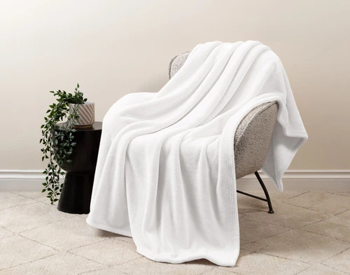 Our Velvet Plush Throw in ____ draped over a beige chair in a white living room.