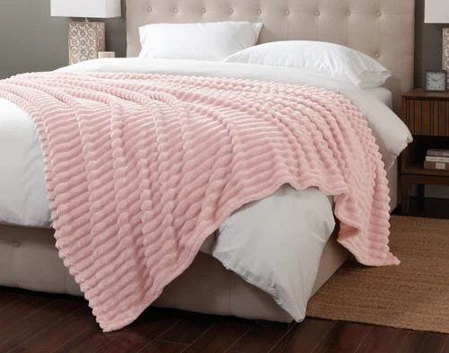 Angled view of our Primrose Ribbed Plush Blanket draped over the corner of a white queen bed.