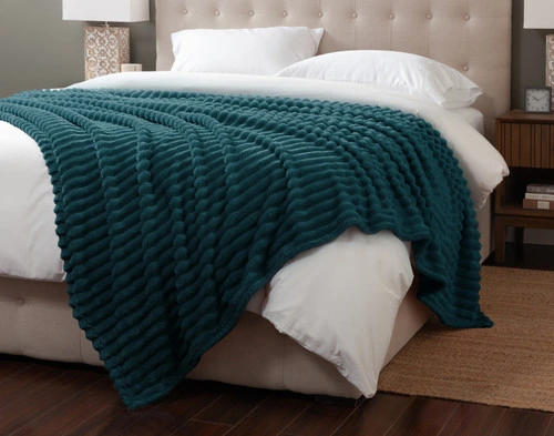 Angled view of our Coastal Ribbed Plush Blanket draped over the corner of a white queen bed.