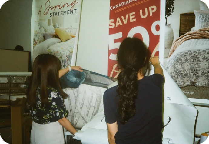 Two QE Home graphic designers adjust store signage in the signage testing area.