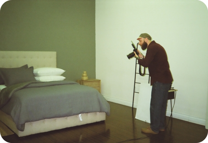 A QE Home photographer crouches behind the camera in one of our photo studios, preparing to capture a shot of our latest bedding design.