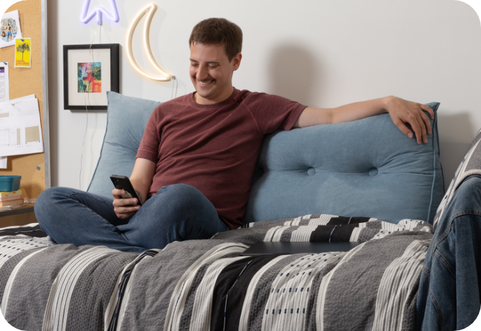 A person rests on their twin bed leaning against our Wedge Pillow in Blue.